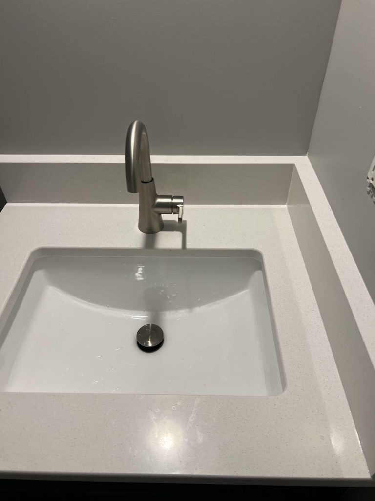8ba8781e-e401-4da3-baca-be74c47d382e A modern bathroom sink with a rectangular white basin, a sleek silver faucet, and a white countertop against a light gray wall.
