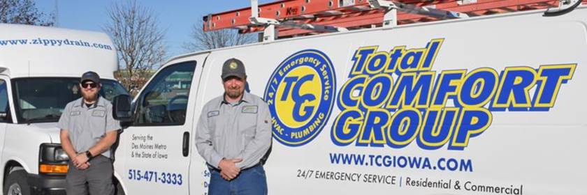 b7232d48-f2d5-484d-80d1-654e0d5da18d Two men in work uniforms and sunglasses stand in front of white service vans labeled "Total Comfort Group" with company logos, website, phone number, and a visible red ladder on the roof.